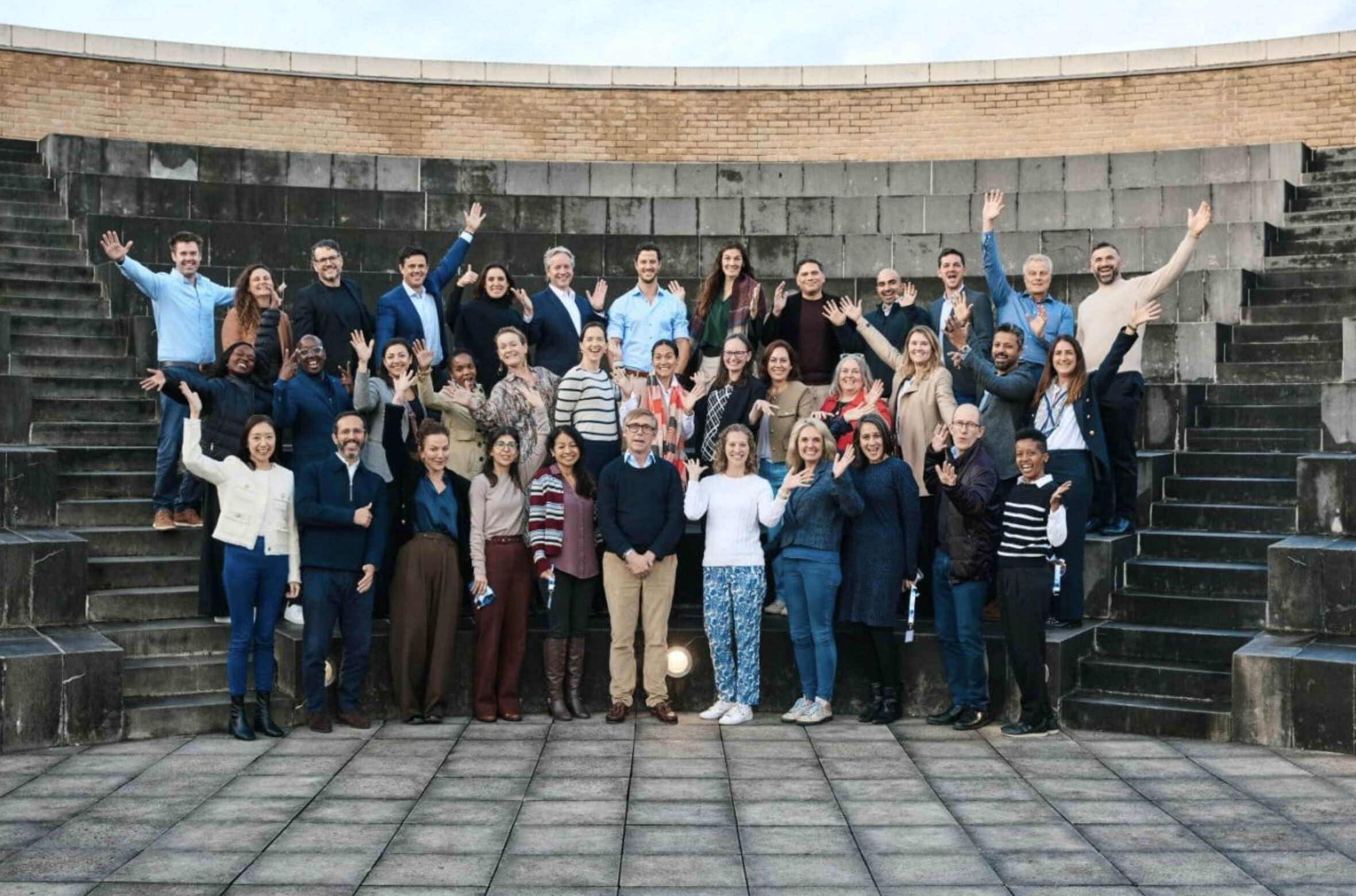 A large group of people waving on the steps of an open-air amphitheatre