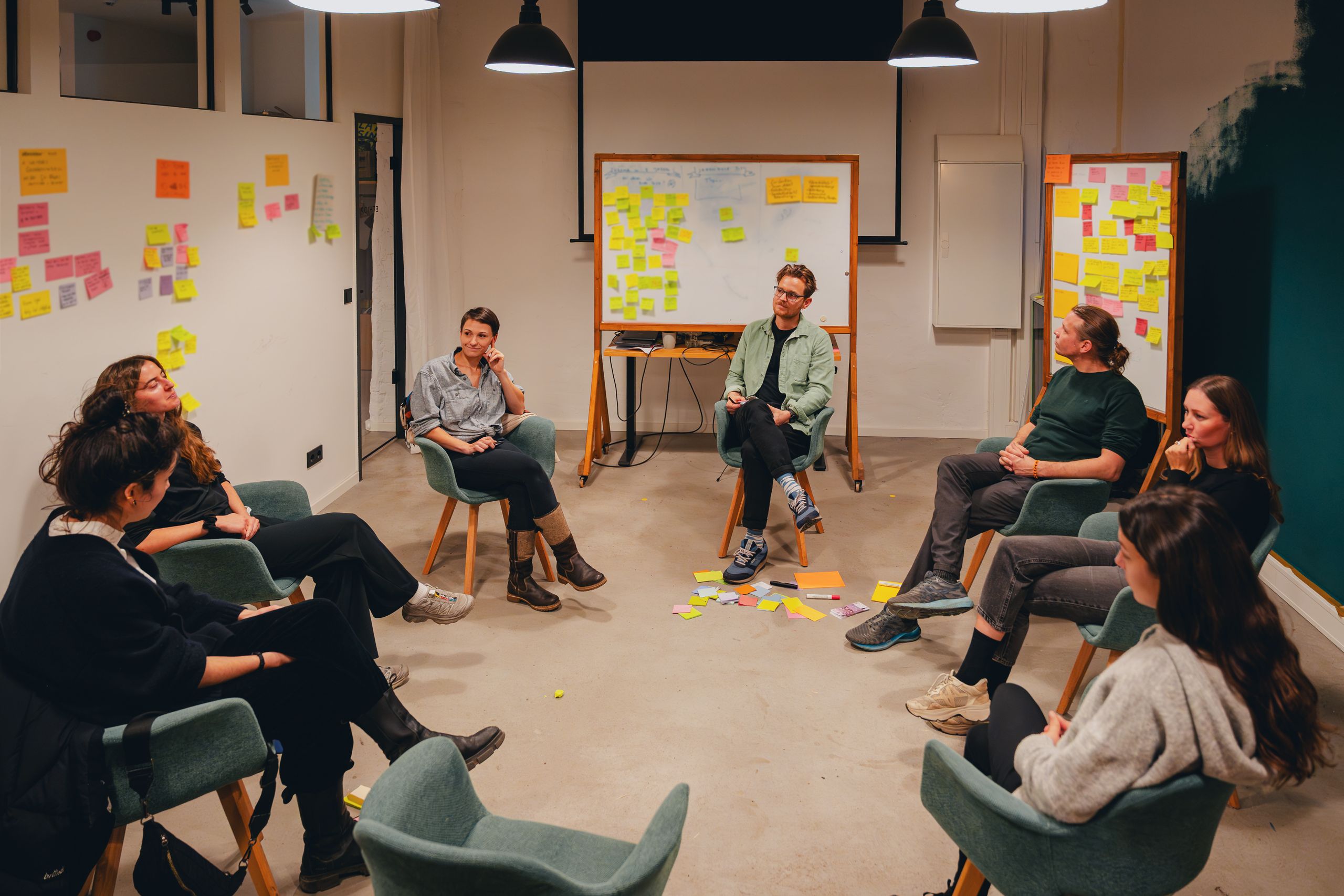 A team seated in a circle of chairs in a workshop room, its walls covered in sticky notes