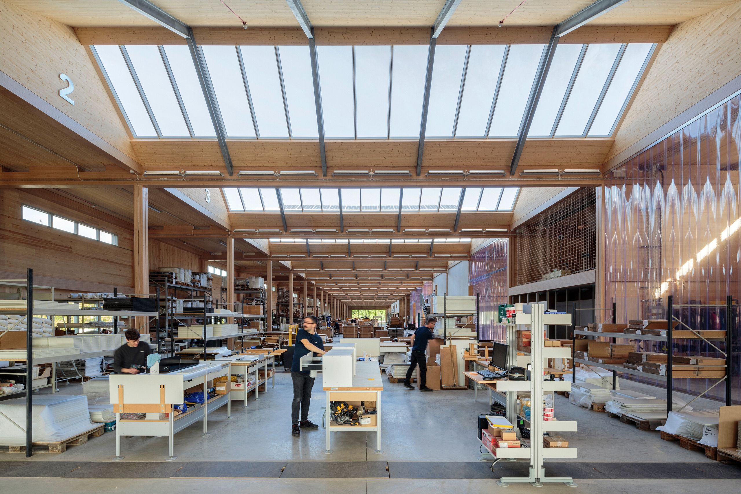 Inside Vitsoe's timber-framed workshop beneath a long skylight, with people at workbenches