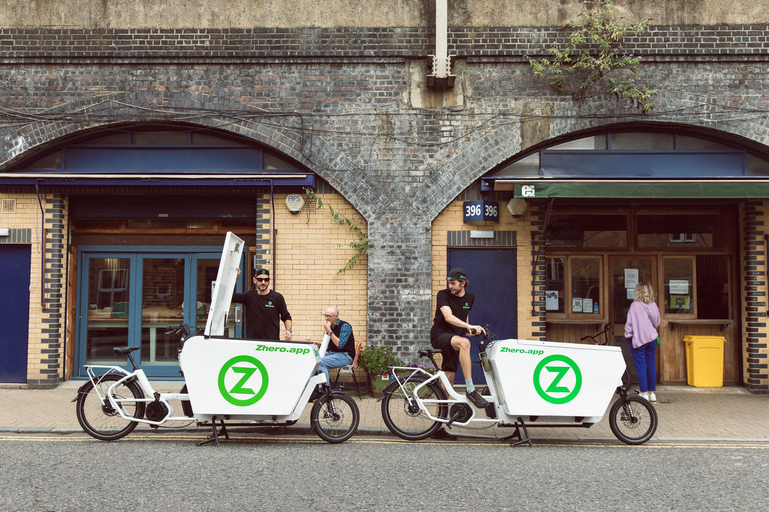 Two riders on white Zhero cargo bikes outside railway-arch workshops
